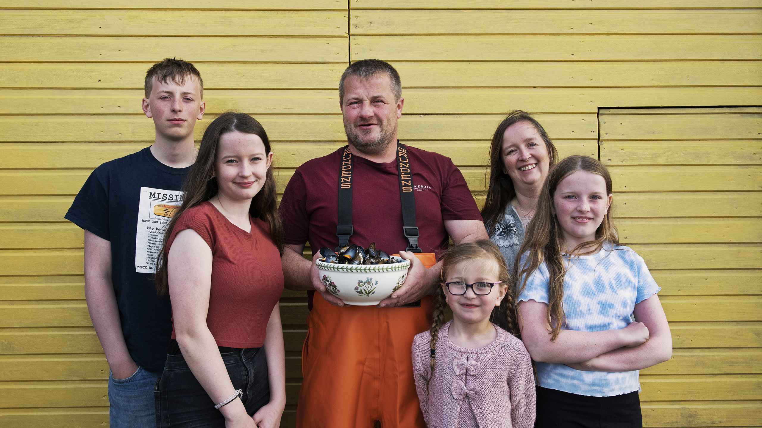 Man holding bowl of mussels surrounded by children